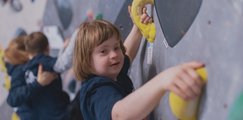 Mädchen beim Bouldern während Kind im hHntergrund von Betreuerin beim Bouldern gehalten wird