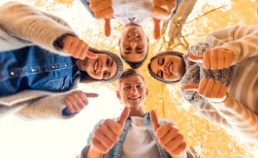 Vier positive, junge Menschen im Kreis mit Daumen hoch