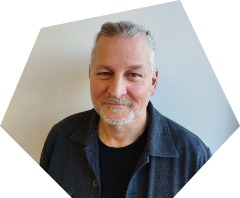 Lächelnder Mann mittleren Alters mit grauen zum Zopf gebundenem Haar, Oberlippen- und Kinnbart