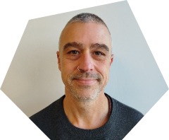 Lächelnder Mann mittleren Alters mit sehr kurzem, grau-schwarzen Haar und Bartstoppeln